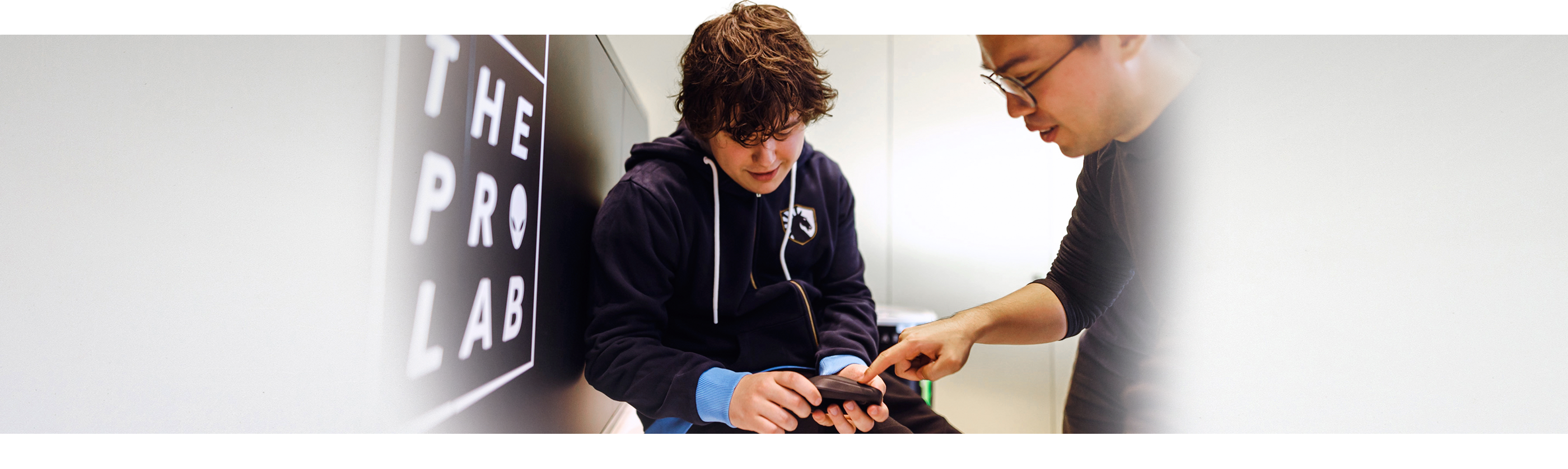 En dreng har en Dell Alienware Pro trådløs gamingmus i hånden, og en mand ved siden af ham peger på produktet.