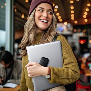 Smiling woman holding a Dell laptop and a Dell Bluetooth Travel Mouse MS700 in her left hand.
