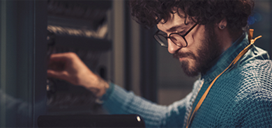 Picture of a man in a blue sweater and glasses with a tablet on the left hand and the right hand on wires on the wall