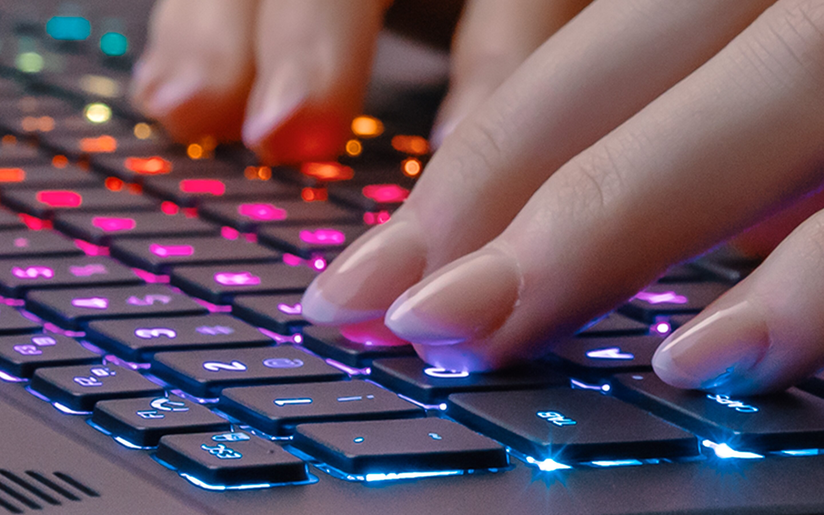 Close-up of fingers typing on a colorful, backlit keyboard. 