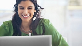 Smiley woman on a green shirt and a headset on her head using a Dell laptop. 