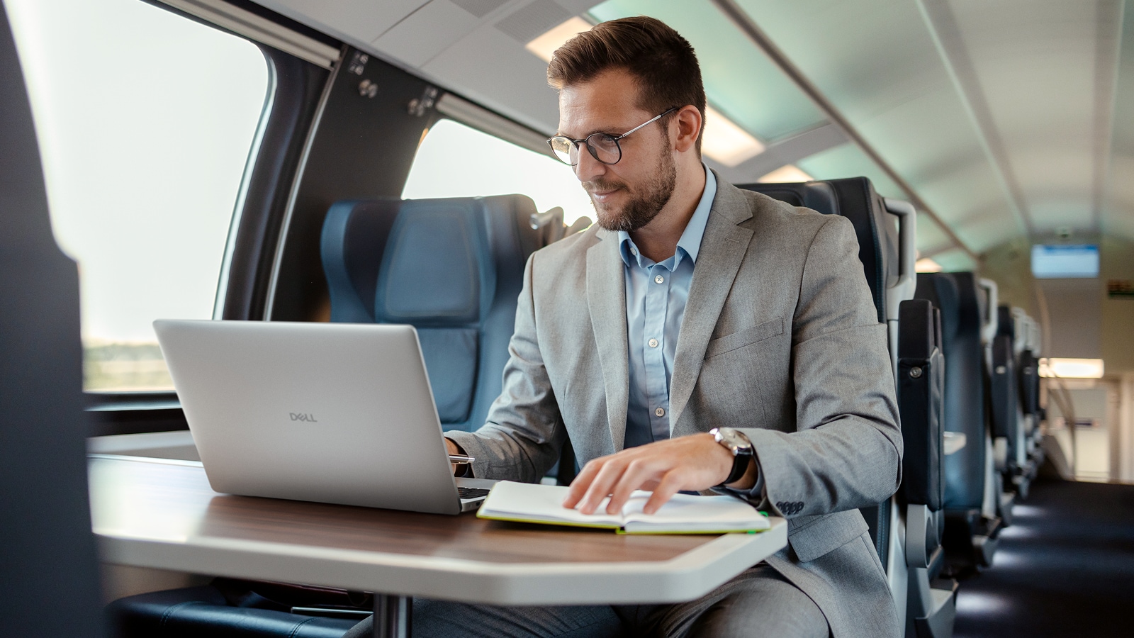 Smiling, bearded man travelling in a train, using a Dell Pro laptop.