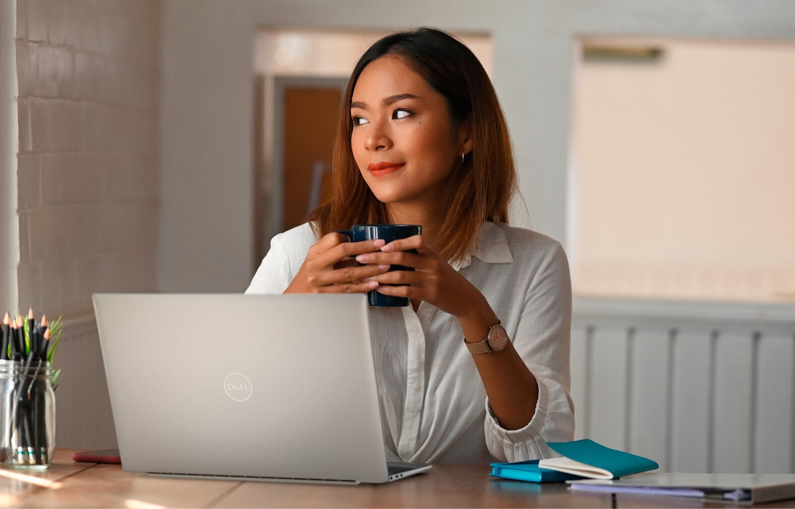 Image d’une femme avec un verre dans les mains qui utilise un ordinateur portable Dell XPS 13 9315 2-en-1 placé sur une table devant elle.