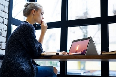 Picture of a sitting woman with a Dell 2-in-1 Laptop opened as a tablet over a wood table in front of her. 