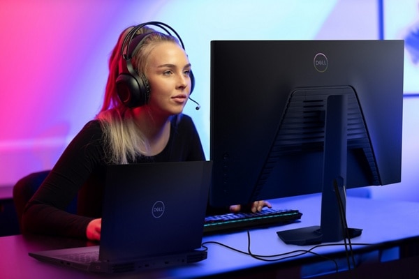 Picture of a sitting woman with a headset on her head and a Dell Monitor, a Dell Laptop, Keyboard, and mouse on a table.