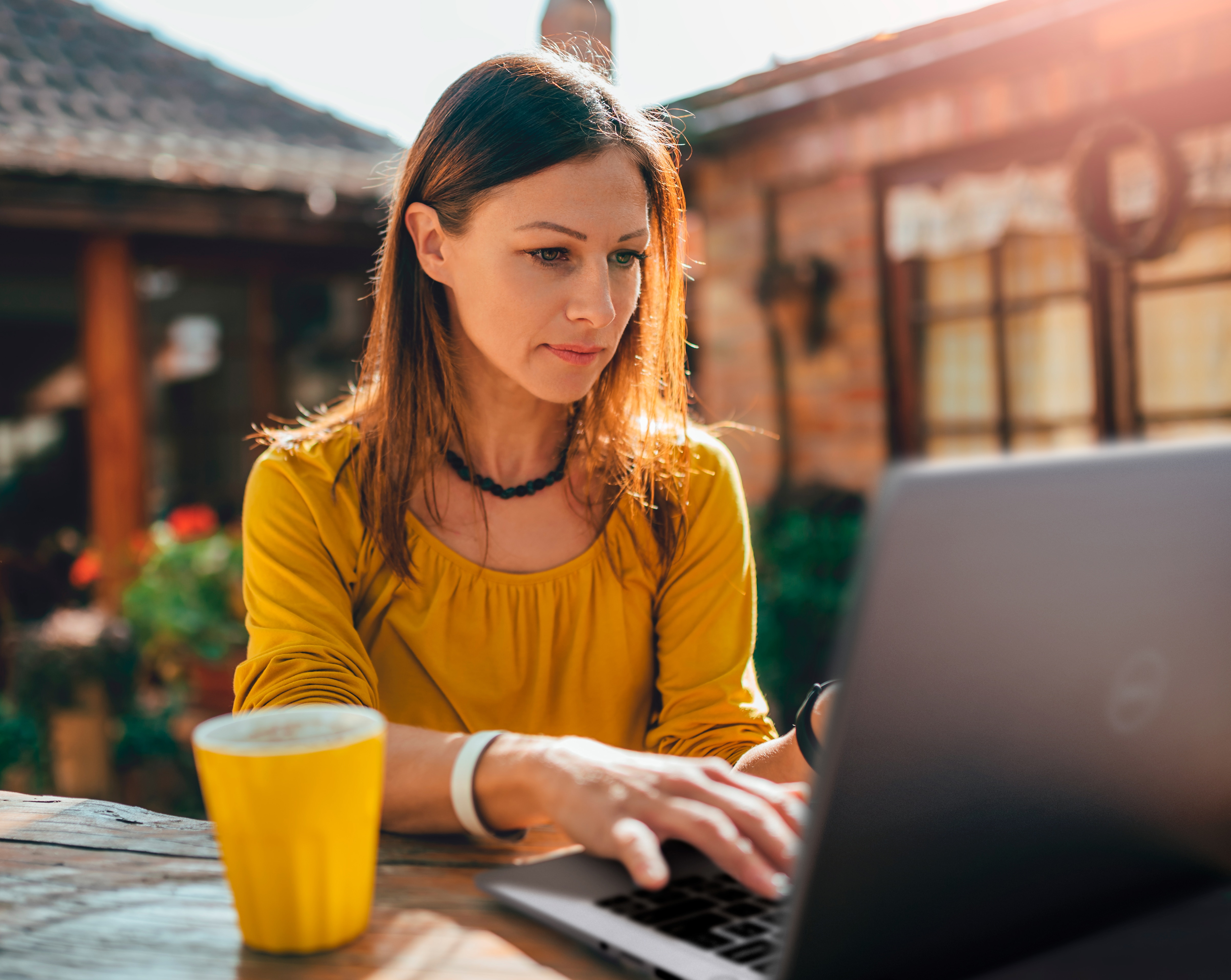 Image d’une femme assise qui porte un chandail jaune et qui utilise un ordinateur portable Dell placé sur une table devant elle aux côtés d’une tasse de café.