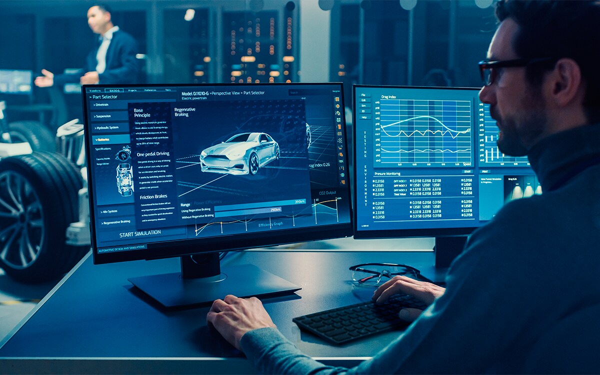 Bild eines Mannes, der einen Monitor, eine Tastatur und eine Maus von Dell auf einem schwarzen Tisch in einem blau beleuchteten Raum verwendet.