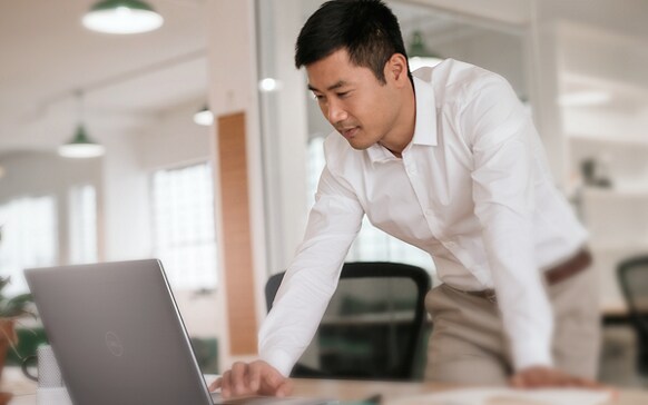 Picture of a man bending over a table with his right hand on a Dell Laptop keyboard on an office room.