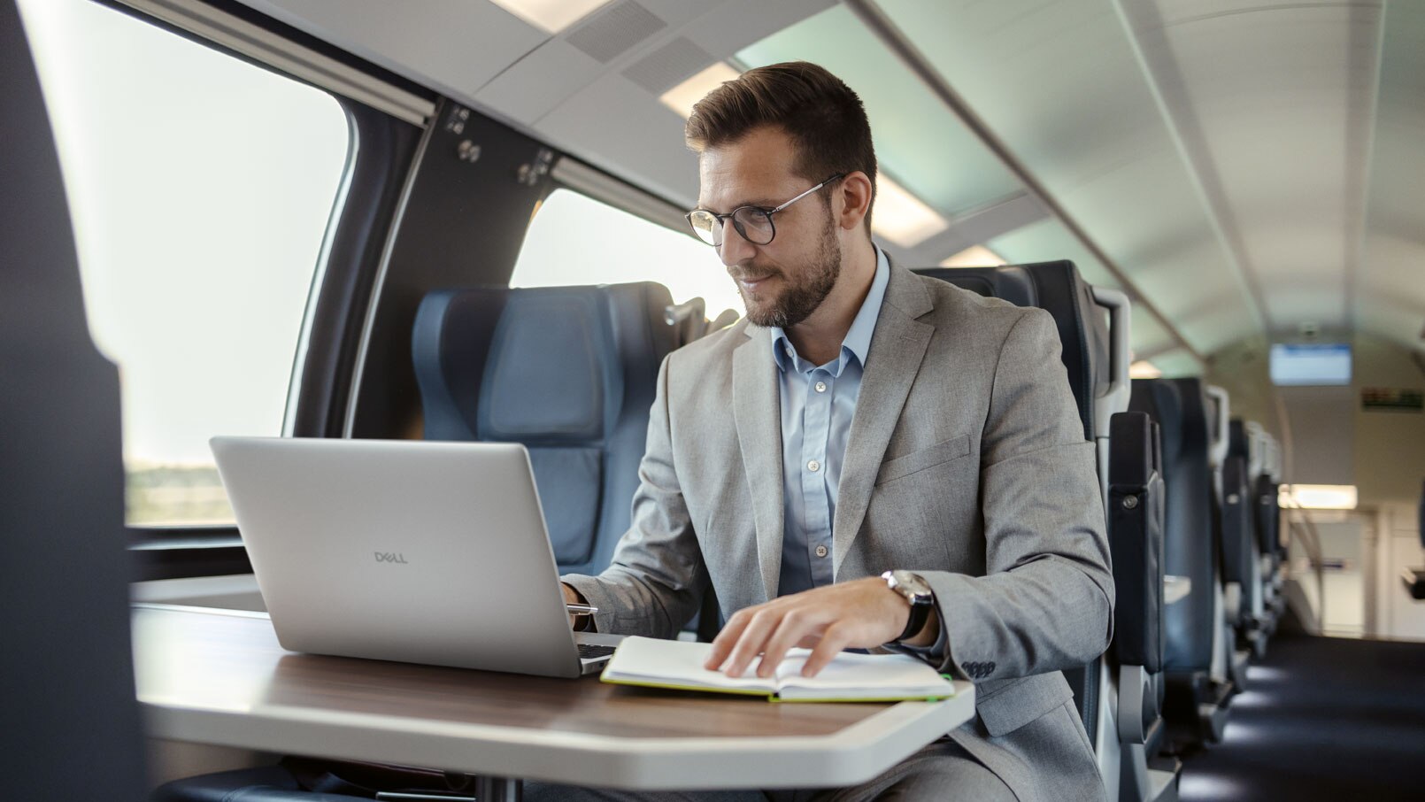 Man in a train using a laptop on a table.
