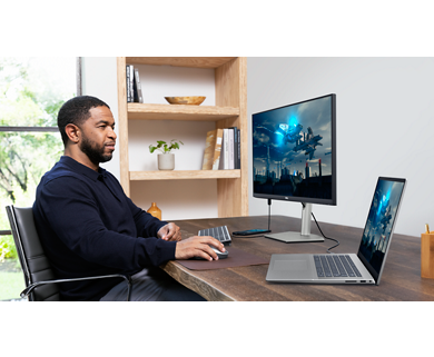 Picture of a man using a Dell S2723HC Monitor connected to a Dell laptop, keyboard, and mouse on a wood table in front of him.