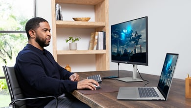 Picture of a man using a Dell S2723HC Monitor connected to a Dell laptop, keyboard, and mouse on a wood table in front of him.