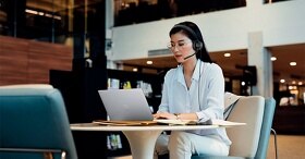 Woman sitting with a headset on her head and using a Dell laptop resting on the table in front of her.