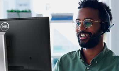 תמונה של אדם מחייך שלובש חולצה ירוקה ומרכיב משקפיים, עם אוזניות על ראשו, משתמש בצג של Dell.