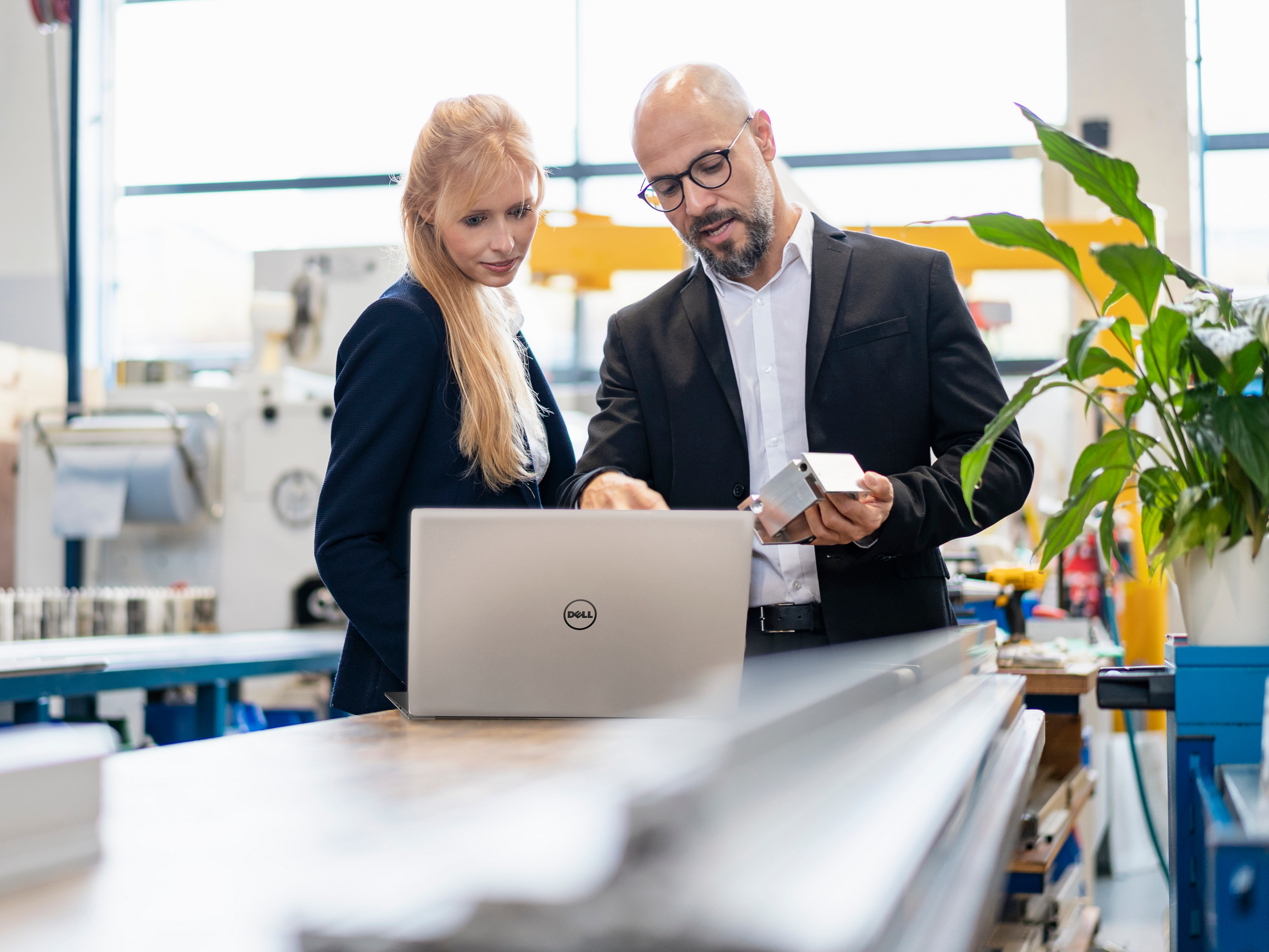 Businessman and businesswoman with laptop and workpiece talking in factory